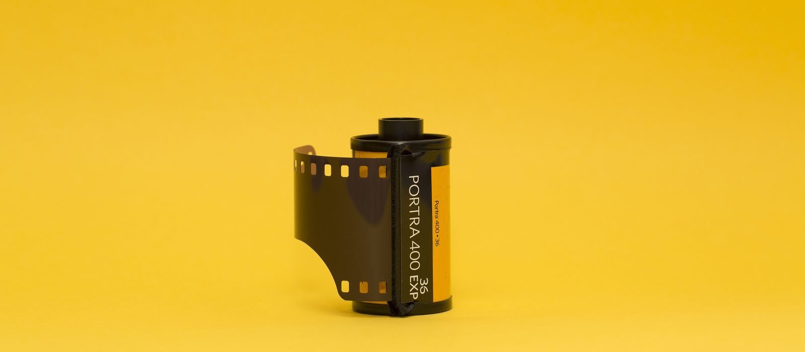 Kleinbild-Filmpatrone mit herausgezogenem Filmstreifen vor gelbem Hintergrund